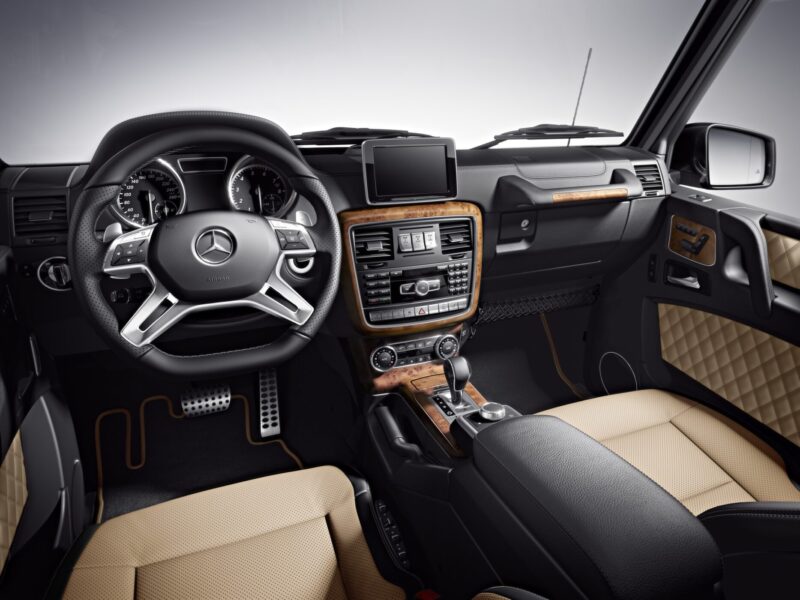 Interior view of a Mercedes-Benz vehicle featuring a leather-wrapped steering wheel, wood trim, beige and black seats, and a central display screen—hinting at luxury touches seen as Mercedes teases the G-Class Cabriolet revival with four doors instead of two.