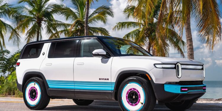 A white Rivian SUV with blue and pink accents is parked on a palm-lined road by the beach—echoing the vibe of the Rivian Opens Brickell Hub With a One-Off Miami-Themed Tri-Motor R1S under a partly cloudy sky.