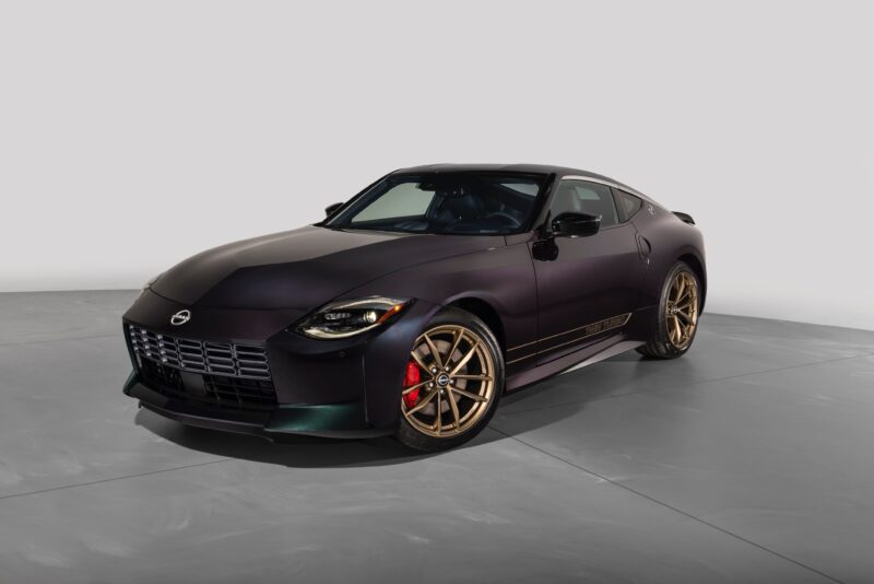 A matte black 2026 Nissan Z Heritage Edition, featuring bronze alloy wheels and red brake calipers, is parked in a well-lit studio with a plain gray background, showcasing its 300ZX-inspired design elements.