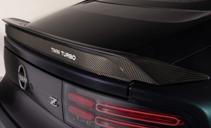 Close-up of the rear end of a 2026 Nissan Z, showcasing the carbon fiber spoiler with "Twin Turbo" text and distinctive taillights inspired by the classic 300ZX-Inspired Design.