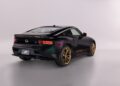 A black Nissan Z Heritage Edition sports car with gold wheels and trim, showcasing its 300ZX-inspired design, is displayed in a well-lit studio and viewed from the rear left side.