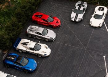 Six luxury sports cars, in blue, silver, red, and white, are parked in two parallel rows on a dark tiled driveway—an impressive lineup sure to captivate luxury car buyers and enthusiasts alike.