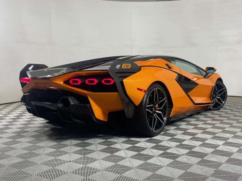 Orange and black Lamborghini Sián Coupe shown from the rear in a well-lit showroom with patterned flooring, highlighting its striking Arancio Atlas finish.