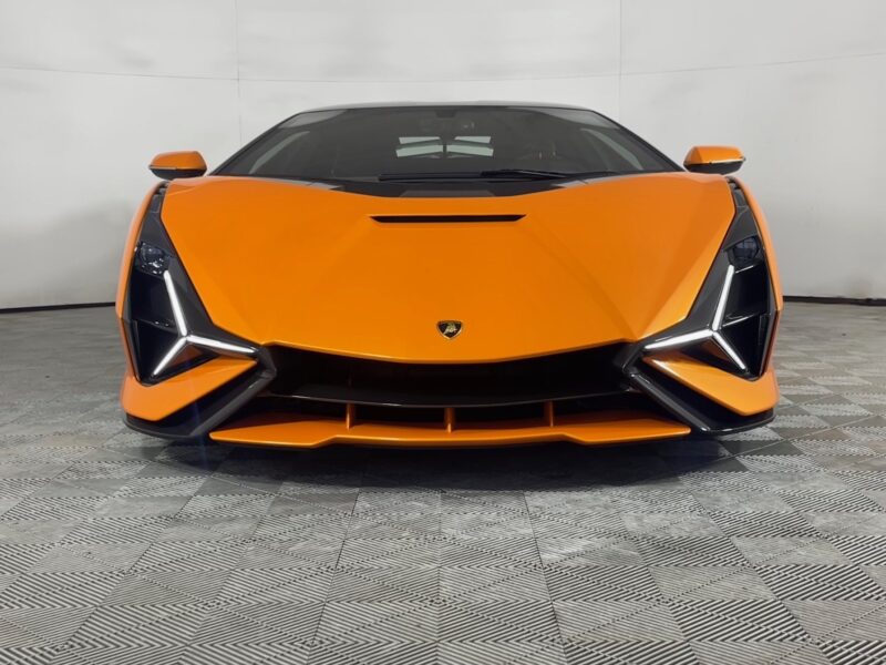 A front view of an Arancio Atlas Lamborghini Sián with sharp, angular headlights, parked indoors on a patterned floor, perfectly capturing the allure of this stunning sports car for sale.