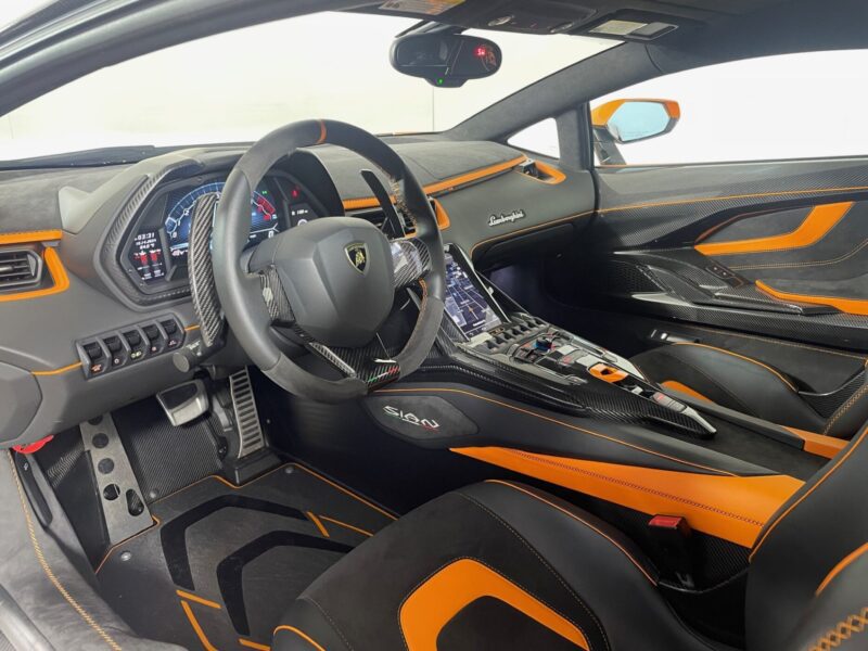 Interior of a 2020 Lamborghini Sián showing the steering wheel, digital dashboard, infotainment system, and black leather seats with orange accents and stitching—luxury details in this extraordinary Lamborghini for sale.