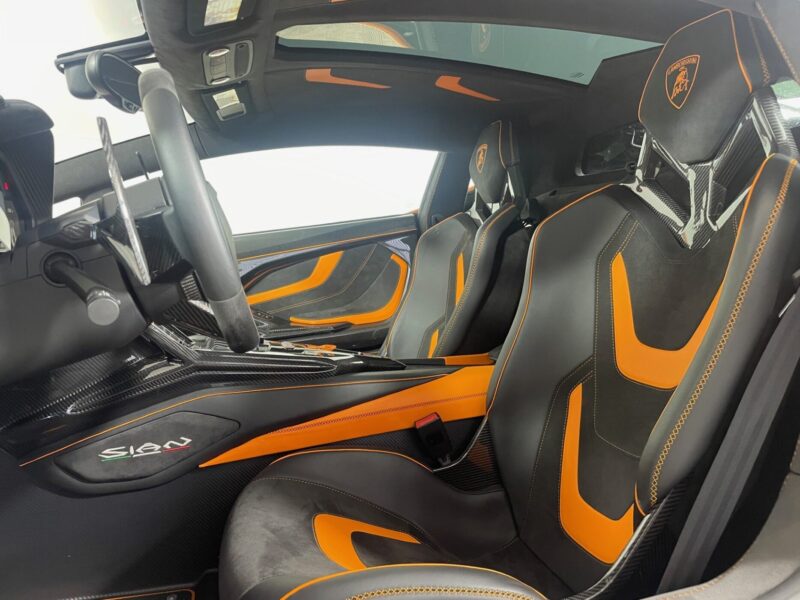 Interior view of a Lamborghini Sián For Sale, featuring black and Arancio Atlas orange leather seats, carbon fiber details, and a modern dashboard.