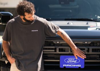 A man places a blue "Ford Racing" license plate on the front of a black Ford truck, proudly showcasing his passion for Ford Performance.