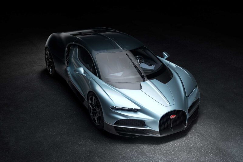 A silver Bugatti Tourbillon sports car is parked on a dark surface, viewed from above at an angle, showcasing its sleek aerodynamic design and distinctive front grille amid a fusion of cutting-edge engineering and rich history.