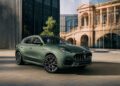 A green Maserati Grecale Folgore EV SUV is parked on a paved area in front of modern glass buildings and a historic stone facade.