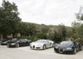 Four legendary Bugatti Veyron sports cars parked side by side on a concrete driveway, surrounded by trees and greenery in an outdoor setting.