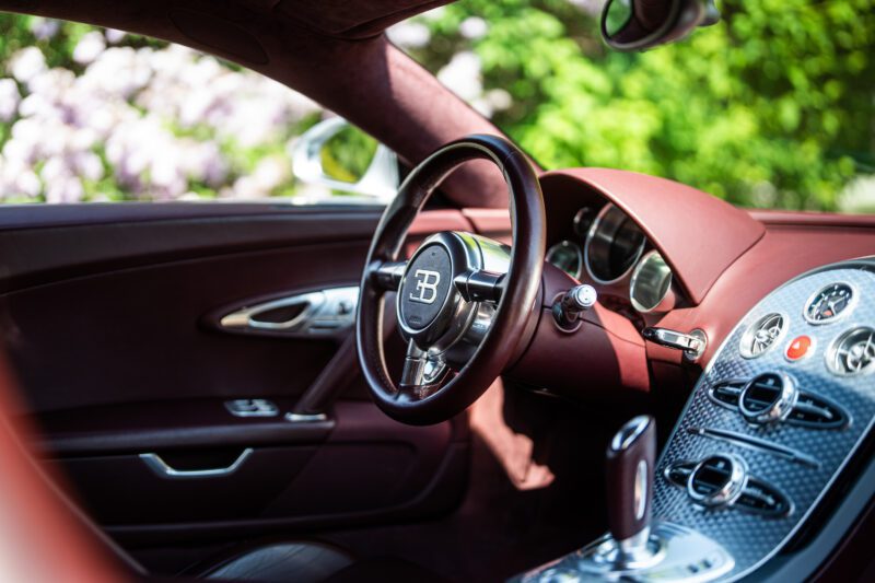 Close-up view of a Bugatti Veyron car interior showing a brown leather steering wheel, dashboard with metallic accents, and control buttons.