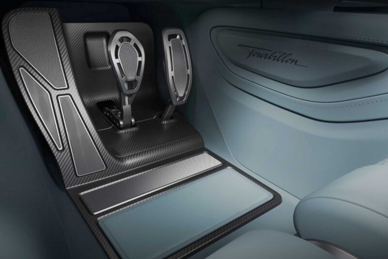 A close-up view of a car's luxury pedal setup with metallic and carbon fiber accents, featuring the word "Bugatti Tourbillon" on the side panel.