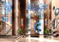 Luxurious hotel lobby at Aureum Estate featuring high ceilings, wood panel walls, striking blue glass chandeliers, a modern stairway, mirrors, decorative sculptures, and lush green potted plants.
