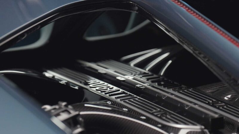 Close-up view of a Bugatti engine cover, highlighting metallic details and the Bugatti logo—showcasing how form, function, past and the future came together in the Bugatti Tourbillon under the car’s hood.