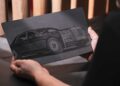 A person holds a rectangular plaque featuring an etched illustration of a luxury car, celebrating Rolls-Royce Honors 100 Years Of Phantom With Groundbreaking Private Collection.