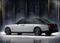 A two-tone luxury sedan with a black roof and white body, part of the Rolls-Royce Honors 100 Years Of Phantom With Groundbreaking Private Collection, is parked indoors against a dark, blurred background with vertical light streaks.