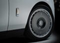 Close-up of a Rolls-Royce car wheel and logo badge, showcasing the vehicle's rim design and part of the white body as Rolls-Royce honors 100 years of Phantom with a groundbreaking private collection.