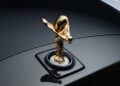 Close-up view of a gold Spirit of Ecstasy hood ornament mounted on the hood of a black Rolls-Royce, as Rolls-Royce honors 100 years of Phantom with a groundbreaking private collection.