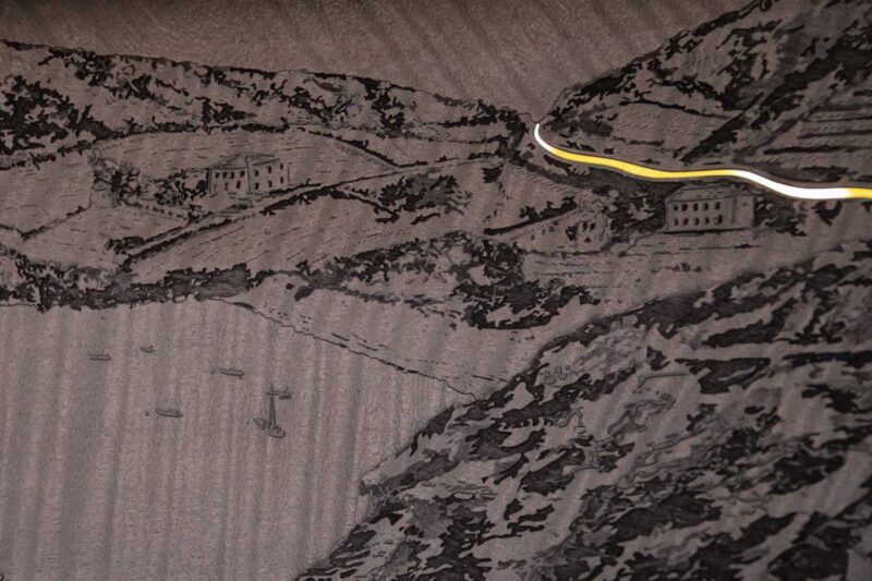 A textured black surface with raised patterns depicting hills, buildings, and boats, intersected by a yellow and white cord near the top right—echoing the elegance of Rolls-Royce Honors 100 Years Of Phantom With Groundbreaking Private Collection.