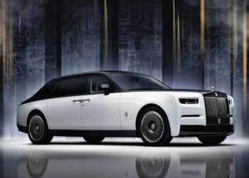 A white Rolls-Royce Phantom luxury sedan with black accents is parked indoors against a dark, illuminated background, celebrating Rolls-Royce Honors 100 Years Of Phantom With Groundbreaking Private Collection.