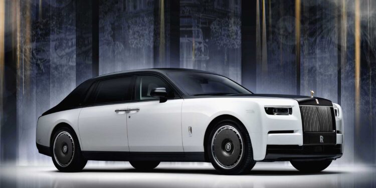 A white Rolls-Royce Phantom luxury sedan with black accents is parked indoors against a dark, illuminated background, celebrating Rolls-Royce Honors 100 Years Of Phantom With Groundbreaking Private Collection.