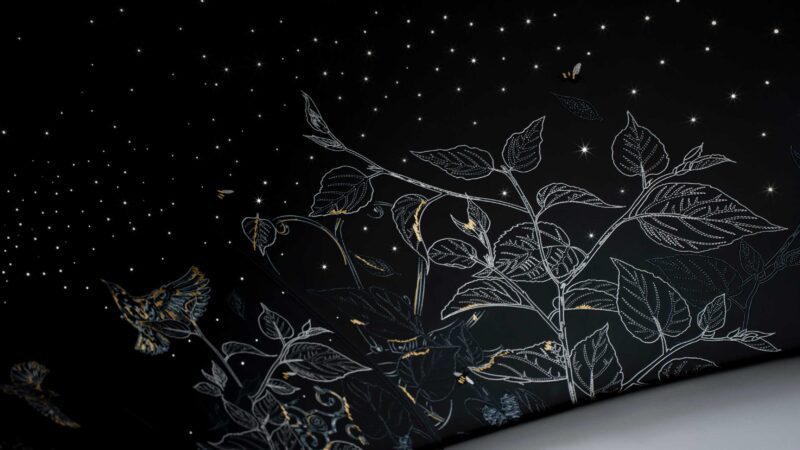 A black wall features intricate line drawings of plants, birds, and butterflies, with small glowing star-like lights above—evoking the elegance of the Rolls-Royce Honors 100 Years Of Phantom With Groundbreaking Private Collection.