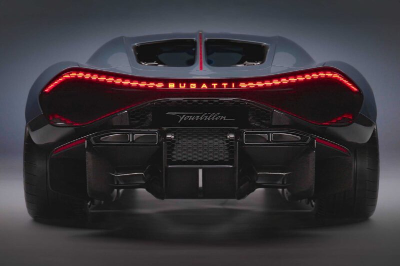 Rear view of a dark-colored Bugatti Tourbillon sports car with illuminated red tail lights and prominent exhaust detailing—here's how nature and history shaped the Bugatti Tourbillon's striking design.