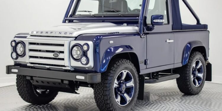 A unique creation: a blue and silver two-door SUV with off-road tires and a soft top roof, parked indoors on a checkered garage floor.