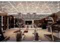 Modern gym interior at Aureum Estate with exercise machines, wooden shelves lining the walls, and a geometric patterned ceiling featuring integrated LED lighting.