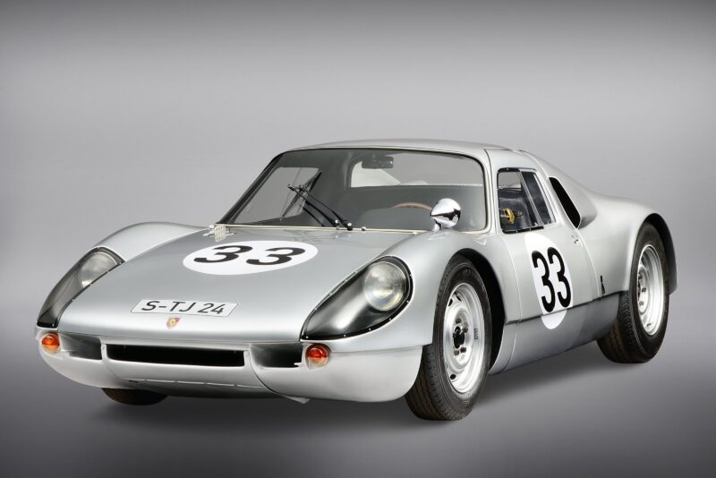 A classic silver race car with the number 33 on the hood and doors, featuring a low, aerodynamic body inspired by Aerfal Automotive's distinctive automotive vision, plus a front license plate reading S-TJ 24, displayed against a plain background.