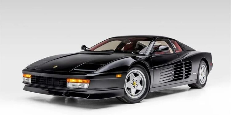 A black Ferrari Testarossa exotic car is parked in a studio setting with a neutral gray background.