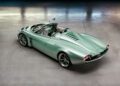 A light green convertible sports car with retro-futuristic design, shown from the rear with an open cockpit and distinctive tail lights, parked on a concrete floor.