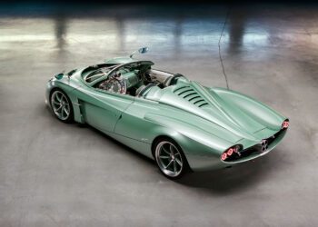 A light green convertible sports car with retro-futuristic design, shown from the rear with an open cockpit and distinctive tail lights, parked on a concrete floor.