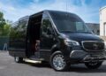A black Sprinter Serenus Plus luxury van with an open sliding door and visible red interior seats is parked outdoors on a sunny day.