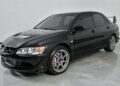 A black Mitsubishi Lancer Evolution sedan with tinted windows, alloy wheels, a hood vent, and a rear spoiler—one of the best manual transmission cars for sale—parked in a plain indoor setting.