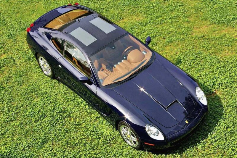 A dark blue sports car with a tan interior and sunroof, possibly one of the 1-of-1: Rarest Ferraris In The World, is parked on grass and viewed from above.