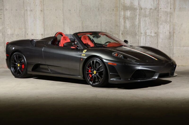 A 2000s Ferrari 430 Scuderia convertible with a striking red interior is parked indoors against a concrete wall—an iconic sports car now for sale.