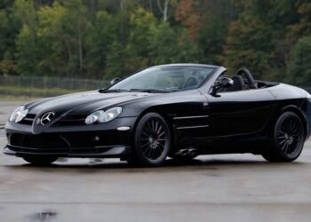 A black Mercedes-Benz SLR McLaren convertible, a true luxury car, is parked on wet pavement with trees in the background.