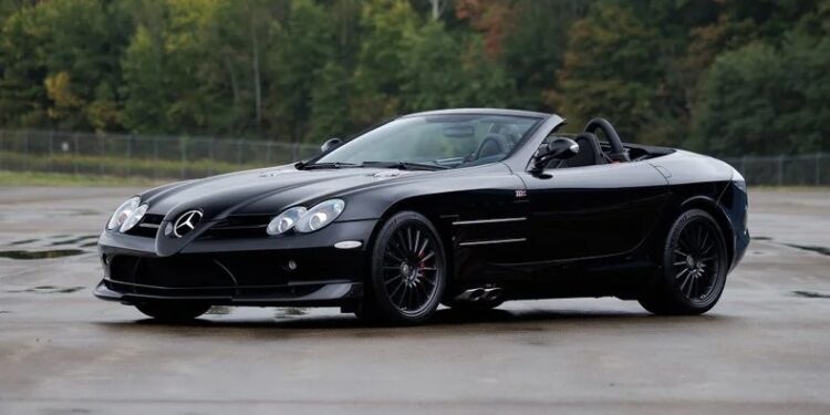 A black Mercedes-Benz SLR McLaren convertible, a true luxury car, is parked on wet pavement with trees in the background.