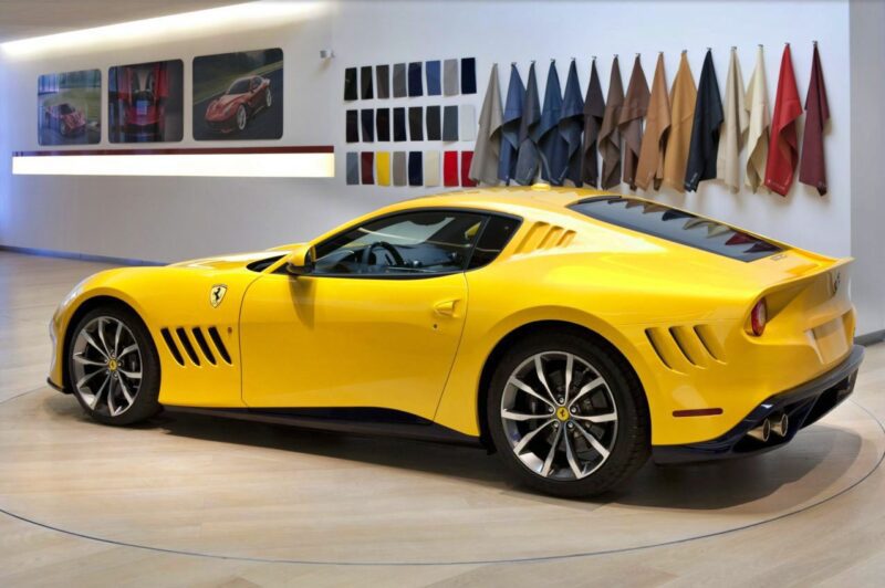 A yellow Ferrari sports car, part of the exclusive 1-of-1: Rarest Ferraris In The World, is parked indoors near a wall displaying various color and leather material samples.