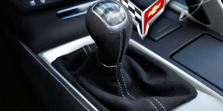 Close-up of a manual gear shift in a car, showcasing the Corvette logo near the lever—highlighting the craftsmanship of this Manual Production Corvette with dashboard controls visible in the background.