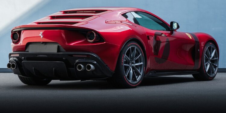 A red Ferrari sports car, one of the 1-of-1: Rarest Ferraris In The World, is parked on a smooth surface, shown from the rear side angle against a plain light blue wall.