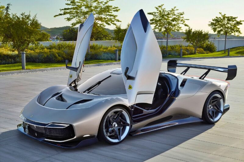 A silver sports car with its scissor doors open is parked on a paved surface near trees and greenery, showcasing the elegance of a 1-of-1: Rarest Ferraris In The World.