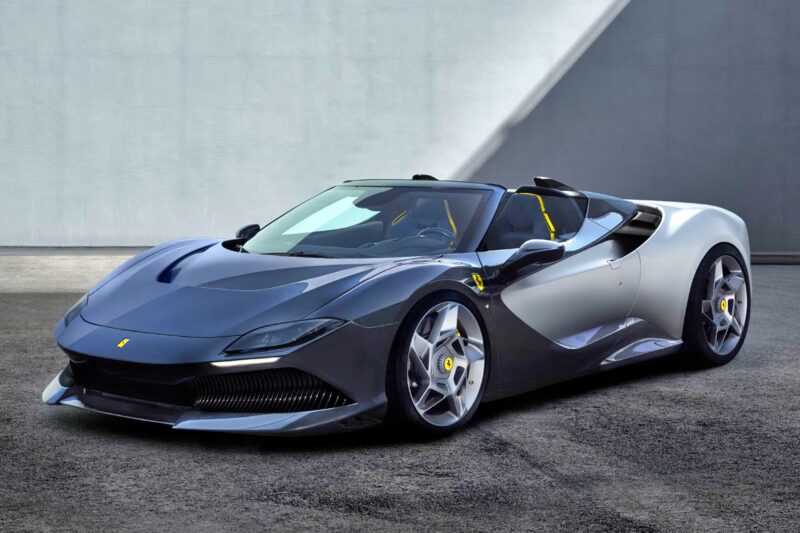 A sleek, gray Ferrari convertible—an exclusive 1-of-1: Rarest Ferraris In The World—is parked on a paved surface in front of a modern concrete wall.