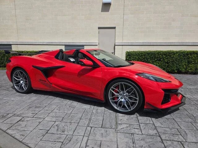 A red luxury convertible sports car with a black interior is parked on a stone-paved surface in front of a beige brick wall and trimmed green hedges.