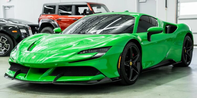 A bright green Ferrari with black wheels is parked indoors on a concrete floor near other vehicles, showcasing one of the bold Ferrari colors.