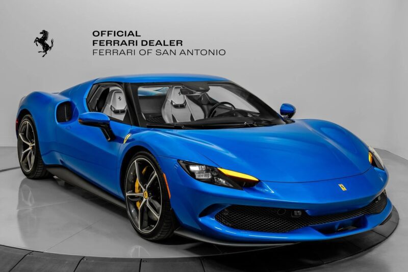 A blue Ferrari, showcasing signature Ferrari colors, is displayed in a showroom with "Official Ferrari Dealer Ferrari of San Antonio" on the wall behind it.