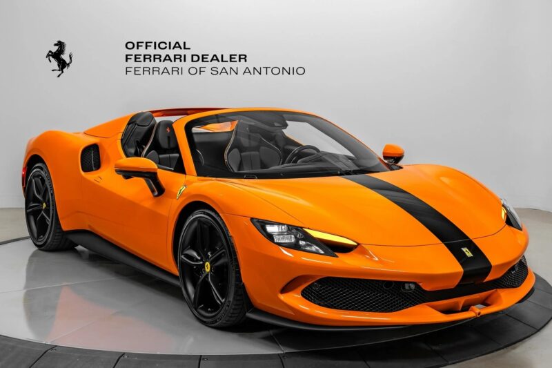 An orange Ferrari with a black racing stripe, showcasing one of Ferrari’s vibrant colors, is displayed in a showroom with "Official Ferrari Dealer Ferrari of San Antonio" on the wall behind it and is available for sale.