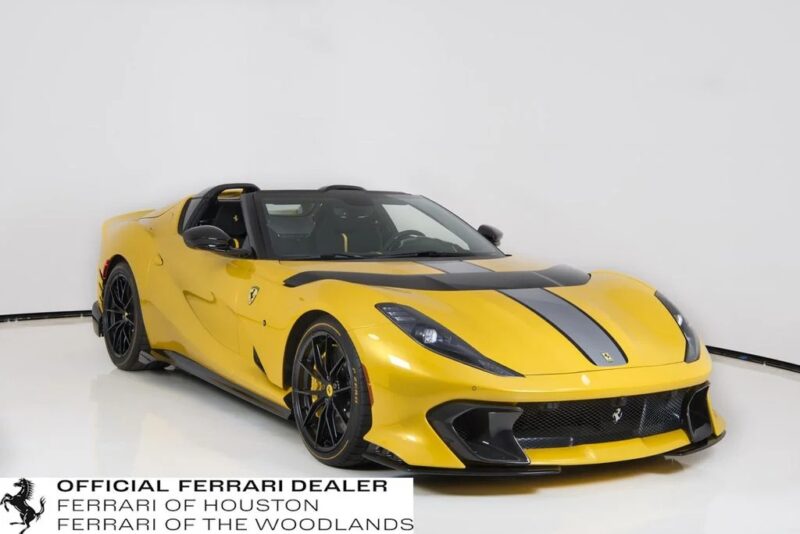 A yellow Ferrari sports car with black racing stripes is parked in a white studio. Sign reads "Official Ferrari Dealer, Ferrari of Houston, Ferrari of The Woodlands." This exotic car is an outstanding example of automotive excellence.