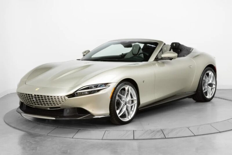 A silver Ferrari convertible sports car, showcasing iconic Ferrari colors, is parked on a rotating platform in a pristine white studio setting.